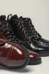 Borcego de cuero vacuno con acabado charol color negro, con cordones y suela de goma.