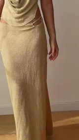 Falda larga tejida color vino tinto con brillo dorado, de corte ajustado y abertura lateral en la pierna.