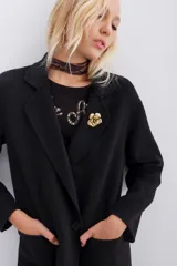Tapado negro de paño sin forrar, de corte holgado, con solapas, cierre cruzado con doble botón y bolsillos aplicados. Incluye pin metálico dorado con diseño floral en la solapa.