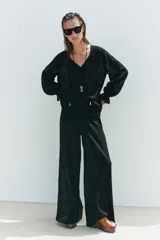 Blusa negra semitransparente con escote en pico, cordón ajustable y mangas largas con elástico en los puños.