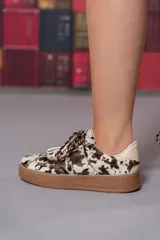 Championes de cuero con estampado animal print de vaca, doble cordón, suela color caramelo y detalle de marca en el talón.