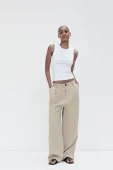 Pantalón color beige de tiro medio con trabillas, pliegues frontales y corte ancho.