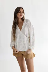 Camisa blanca de tela de punto bordada con manga corte ranglan abuchonada, escote en V y cuerpo que se cierra cruzado atada con lazos.