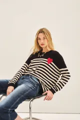 Sweater de punto a rayas horizontales en blanco y negro, con detalle de corazón rojo en el pecho.