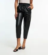 Pantalón zanahoria color marrón claro confeccionado en material sintético con cintura elástica, cordón ajustable con punteras metalizadas, bolsillos laterales y traseros.