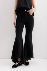 Pantalón de jean negro elastizado con corte ajustado y volados en la parte baja de la pierna. El ruedo es más largo en la parte trasera y tiene terminación descosida.