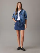 Campera de denim azul medio vintage, corte relaxed boxy, confeccionada con 20% de algodón reciclado. Tiene cuello en punta, bolsillos de parche en el pecho, bolsillos de hendidura en la cintura, botones metálicos de la marca y parche con logo de Calvin Klein en el bolsillo del pecho.