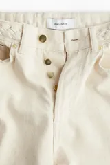 Pantalón de jean color crema, de corte amplio y cintura alta, con detalle de trenzado en la pretina.