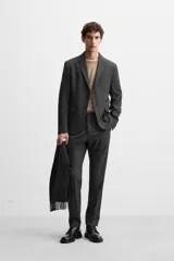 Blazer slim fit color gris oscuro confeccionado en tejido con viscosa. Tiene cuello con solapas de muesca, manga larga con puño abotonado, bolsillo de vivo en pecho, bolsillos de solapa en cadera, bolsillo interior, bajo con aberturas en espalda y cierre frontal con botones.