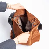 Cartera tipo bucket color marrón de cuero graneado con correa de cuero engrasado negra y hebilla metálica plateada.