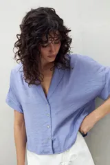 Camisa celeste de manga corta con cuello solapa y botones de nácar al frente, confeccionada en un tejido liviano de sutil textura.