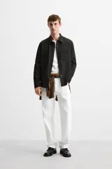 Sobrecamisa negra de tejido con elasticidad, cuello solapa y manga larga acabada en puño con botón a presión. Tiene bolsillos de plastrón en el pecho y cierre frontal con botones a presión.