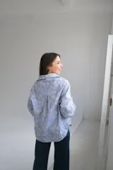 Camisa de manga larga con cuello camisero y escote en pico. Diseño a rayas verticales azules y blancas con bordados florales perforados en blanco en la parte delantera y trasera.