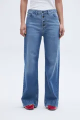 Pantalón jean celeste de corte holgado con pierna ancha y tiro alto. Tiene bolsillos delanteros y traseros, y cierre frontal con botones a la vista.