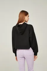 Buzo negro cropped con capucha y mangas largas abullonadas. Estampado frontal con una flor azul y texto en blanco.