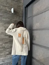 Sweater beige con cuello alto, cierre con presillas de cuero y bolsillos frontales con ribete de cuero.