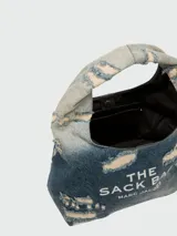 Bolso de hombro Marc Jacobs modelo The Sack Bag, confeccionado en denim azul con efecto desgastado y roturas. Presenta el logo de la marca estampado en el frente.