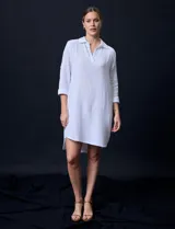 Vestido camisero blanco de algodón con cuello solapa, escote en V y mangas 3/4 regulables. Presenta bolsillos laterales verticales y abertura con botones en la espalda.