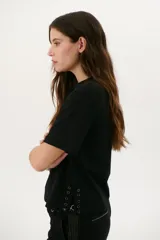 Remera blanca de algodón de corte recto, con cuello redondo y mangas cortas. Presenta detalle de aberturas laterales con ojales metálicos.