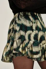 Falda corta con volados, tiro alto, confeccionada en tejido lurex con estampado abstracto en tonos verde oscuro y dorado.