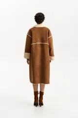 Abrigo largo de diseño envolvente, exterior de cuero gamuzado color marrón y forrería interior de corderito color beige. Presenta solapas anchas de corderito y puños también de corderito.