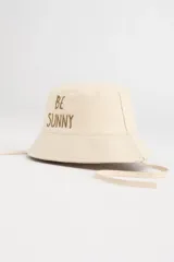 Gorro tipo bucket color beige con bordado frontal de la frase "Be Sunny" en marrón. Incluye cordones laterales ajustables.