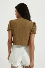 Top corto color mostaza con textura arrugada, escote en V profundo y mangas cortas abullonadas con elástico en el borde. Presenta un ajuste de cordón fruncido en la cintura que se ata con un lazo doble en el frente.