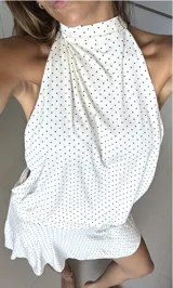 Vestido corto blanco con lunares negros, de algodón, con cuello halter que se ata detrás del cuello y faja en la cintura.