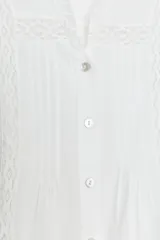 Camisa blanca de cuello subido y manga larga, con detalle de entredós combinados a tono y cierre frontal con botones.
