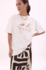 Remera blanca de algodón, corte oversize, con cuello redondo y manga corta. Presenta un estampado frontal con varias reposeras y hamacas de playa, y el texto "LA SIESTA".
