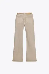 Pantalón de jean color beige, de tiro alto, corte ajustado en la cadera y muslos, y acampanado desde la rodilla. Tiene cinco bolsillos y cierre frontal con cremallera y botón.