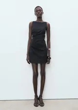Vestido corto negro de corte ajustado, sin mangas y con cuello redondo. Presenta detalle drapeado en la falda.