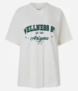 Remera de algodón color crema, de corte amplio y mangas cortas. Presenta cuello en V y estampa frontal con texto en verde y negro.