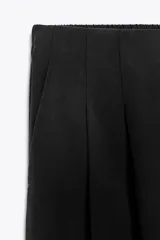 Pantalón palazzo negro de tejido fluido con tiro medio, cintura elástica en la espalda, bolsillos laterales ocultos y pinzas en el delantero.