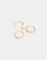 Set de tres anillos dorados con diferentes diseños: uno con strass, otro con detalle de color rosa y uno con una piedra transparente.