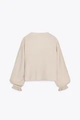 Blusa blanca de cuello solapa y manga larga abullonada terminada en volantes. Presenta bordados florales calados en el frente y cierre frontal con botones.