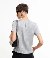Blusa plateada de mangas cortas con cuello redondo pespuntado, botón en la espalda y superficie metalizada.