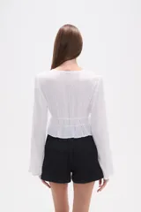 Blusa de rayón color blanco con detalles de broderie, cuello en V y cierre frontal con cordones para atar. Presenta mangas largas y cintura elástica con terminación en volado.