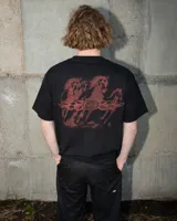 Remera negra de manga corta con estampado serigrafiado en la espalda de caballos galopando en tonos rojizos, con llamas y un logo central ovalado.