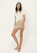 Pijama de dos piezas compuesto por una remera de manga corta color crema con un pequeño bordado de concha marina y un short de tiro alto con elástico y estampado de cuadrícula en tonos beige y blanco.