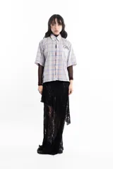 Camisa unisex de manga corta con estampado a cuadros en tonos verde, negro, blanco y morado. Presenta un corte boxy y un estampado en serigrafía en el pecho.