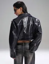 Campera corta de cuero sintético negro con cierre cruzado, cuello con solapas y cinturón con hebilla.