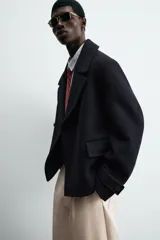 Abrigo corto azul marino de corte relajado, confeccionado en tejido con lana. Tiene cuello con solapas de pico, mangas largas con puños ajustables con trabilla, bolsillos de solapa en la cadera, bolsillo interior, abertura en el centro de la espalda y cierre frontal con botonadura.