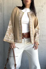 Chaqueta color beige con bordados blancos en el frente y las mangas, de corte recto y mangas anchas.