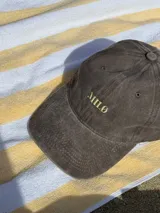 Gorra de béisbol color marrón con bordado frontal de la palabra "MILO" en color dorado.