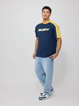 Remera de hombre azul marino con mangas y cuello amarillo, y logo de la marca Rusty estampado en el pecho.