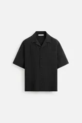 Camisa negra de corte relaxed fit, confeccionada en tejido con mezcla de modal. Tiene cuello bowling, manga corta, bolsillo de parche en el pecho y cierre frontal con botones.