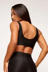Top deportivo negro con textura colmena 3D, escote cuadrado, breteles anchos y banda inferior con logo.