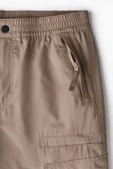 Pantalón cargo color beige de corte recto, con cintura elástica ajustable con cordón, bolsillos laterales con cierre, bolsillos tipo cargo con solapa en los laterales y bolsillos traseros insertados.