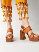 Sandalias de plataforma color naranja con detalles en marrón. Tienen tiras anchas sobre el empeine y el tobillo, y un tacón cuadrado alto.